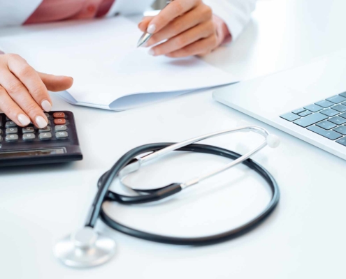 Doctor using calculator writing bills and doing bookkeeping_By Kzenon