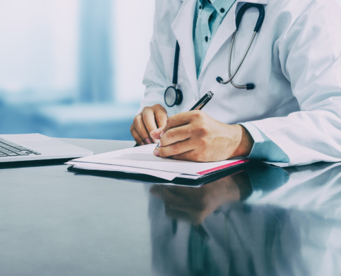 Male doctor sitting at table and writing on a document report in hospital office