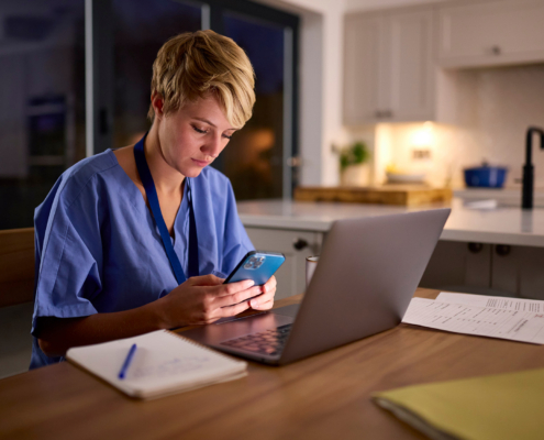 Woman In Medical Scrubs Looking At Mobile Phone Working Or Studying